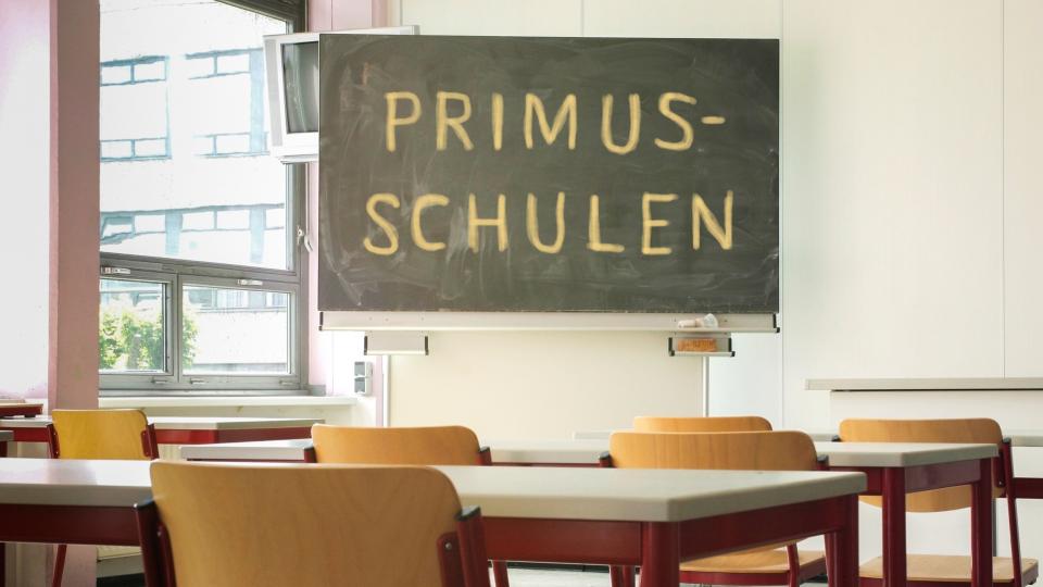 Das Bild zeigt einen leeren Klassenraum, an der Tafel steh Primusschulen.