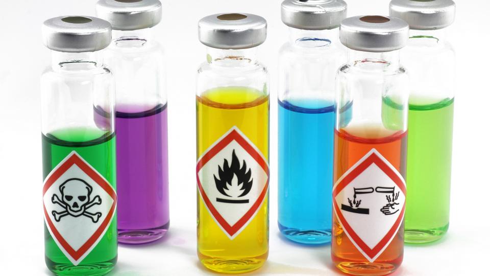 Abgebildet sind sechs Glasbehälter, die toxische, leicht entflammbare und ätzende Flüssigkeiten enthalten. 
