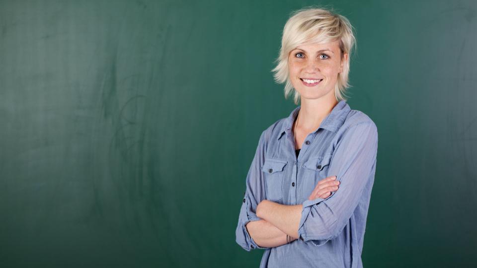 Eine Lehrerin steht vor einer grünen Tafel in einem Klassenraum