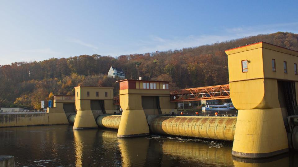Ein Wasserkraftwerk an einem Fluss mit Schiffen im Hintergrund