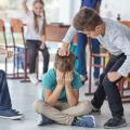 Ein auf dem Boden sitzender und weinender Junge wird von seinen Klassenkameraden gemobbt. Ein Junge zeigt mit dem Finger auf ihn und ein anderer deutet einen Faustschlag an. Ein Mädchen im Hintergrund befürwortet die Aktion ihrer Klassenkameraden. 